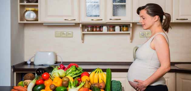 نصائح الأسبوع السادس والعشرين من الحمل، حامل تقف في المطبخ أمامها خضار وفواكه كثيرة